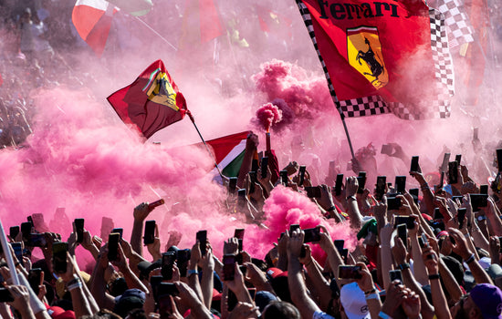 Ferrari fans holding up flags and smoke canisters in a celebratory atmosphere with pink smoke.